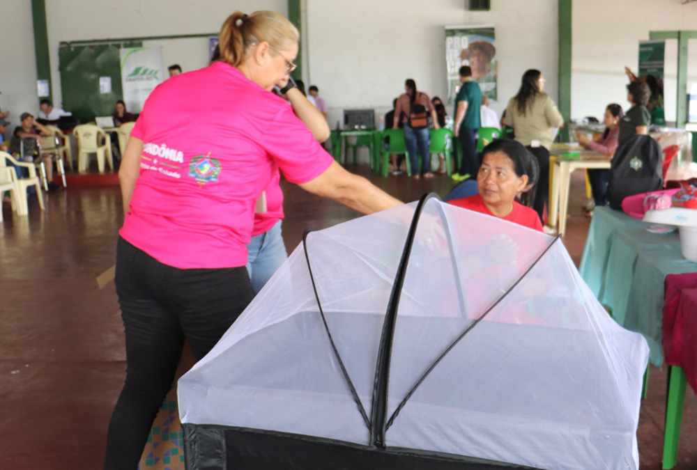 Agente da Seas apresenta o berço com mosquiteiro a mãe beneficiaria do programa mamãe cheguei